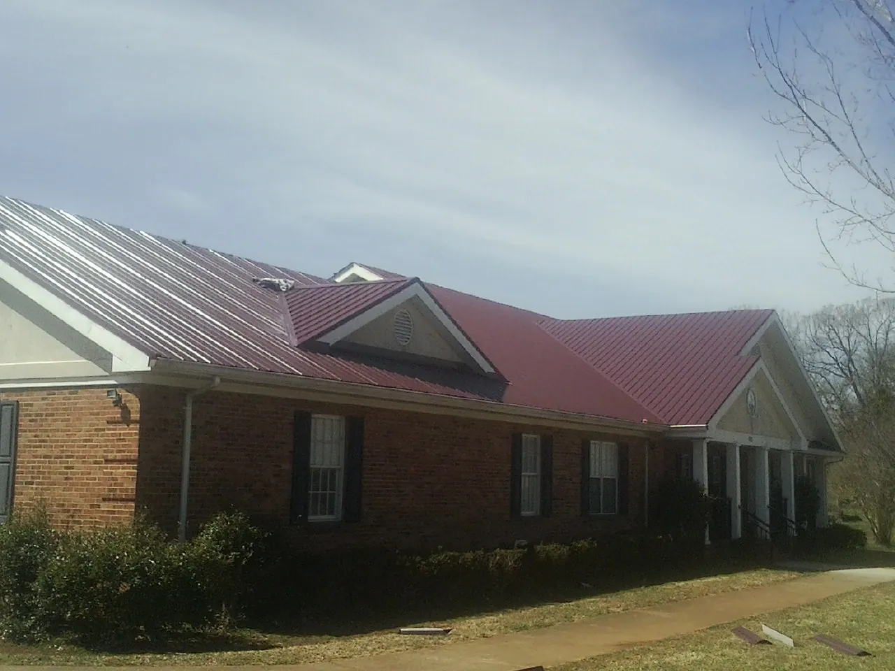 Red metal roof with gabled entries on a long brick building, from a Hail Damage Roof Repair job in Belton