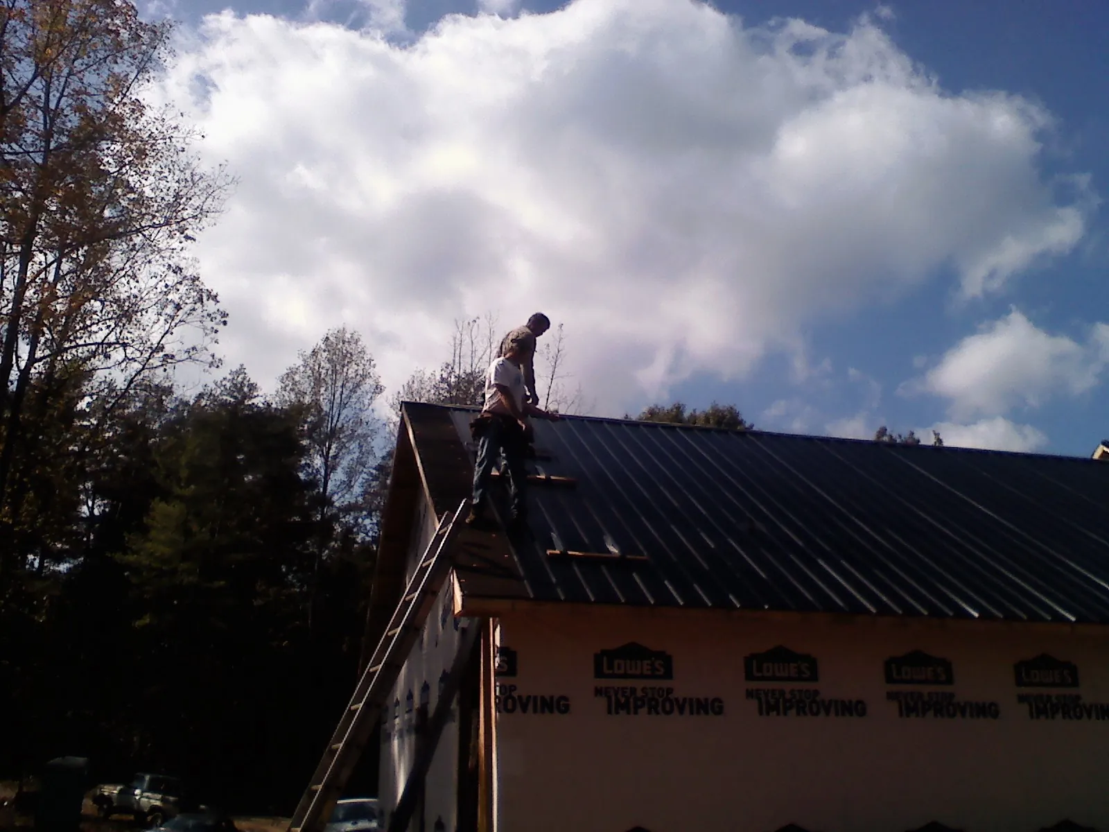 Roofer fastening dark metal panels high against a cloudy sky, from a Roof Inspection job in Belton